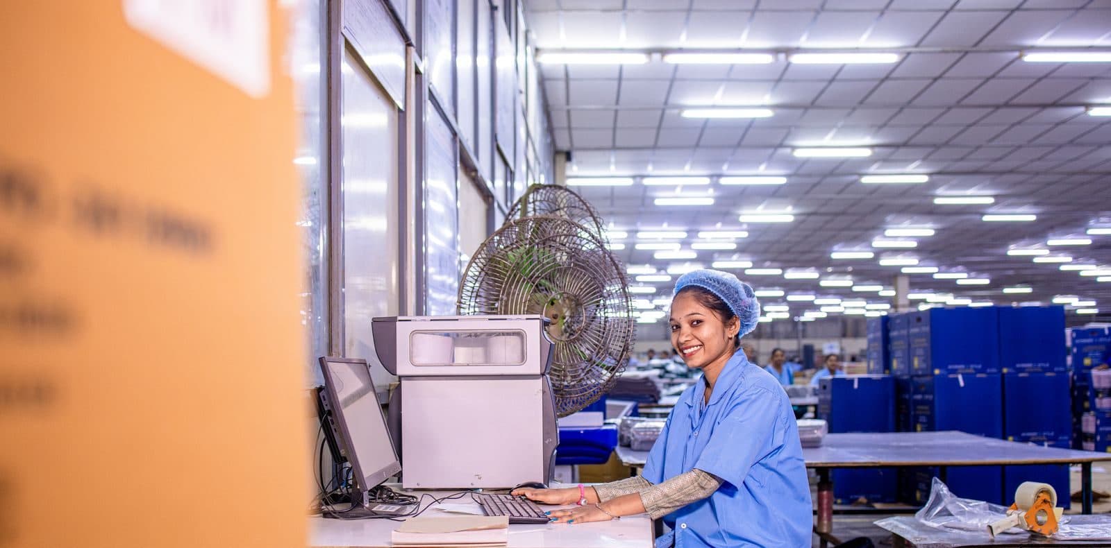 Operadora de uma fábrica sorri ao lado do computador no galpão de produção.